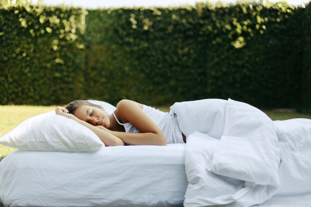 A woman trying to improve sleep quality by sleeping on a white mattress with all-white bedding in a grassy garden