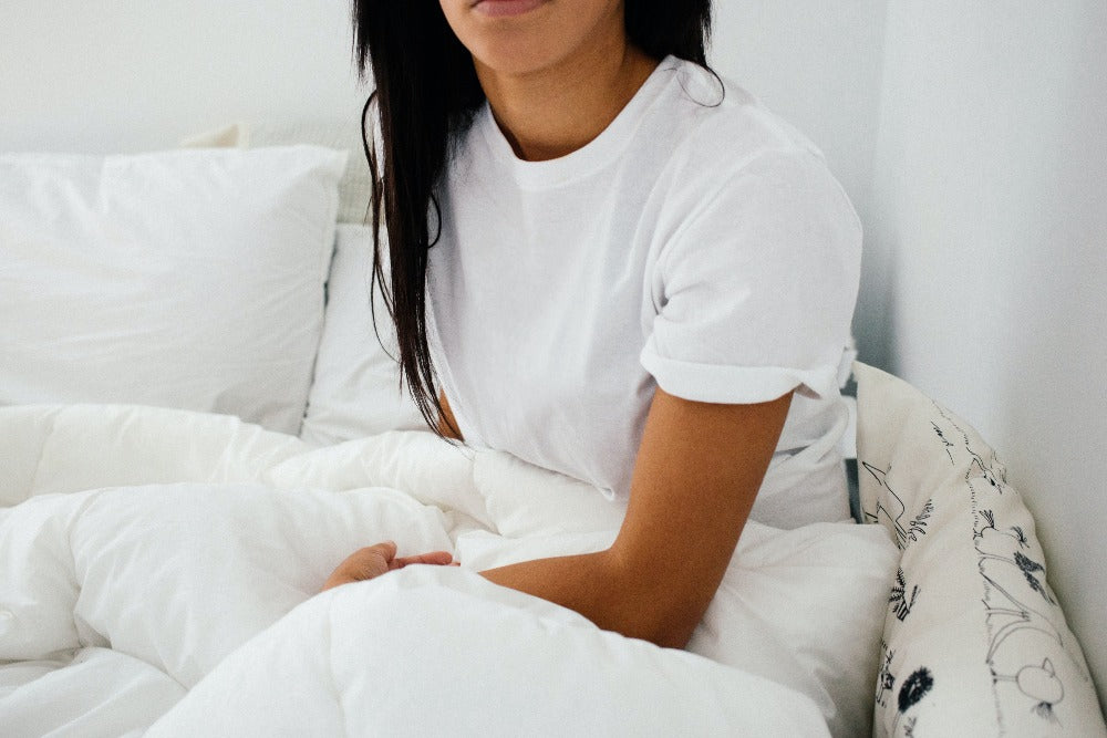 Woman in a white T-shirt waking up from a restful night’s sleep in her white bed